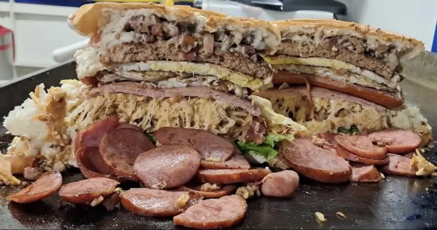 Lanche recheado da Ferracini Lanches, cortado ao meio, mostrando as camadas de carne, queijo, ovo, presunto e linguiça calabresa fatiada